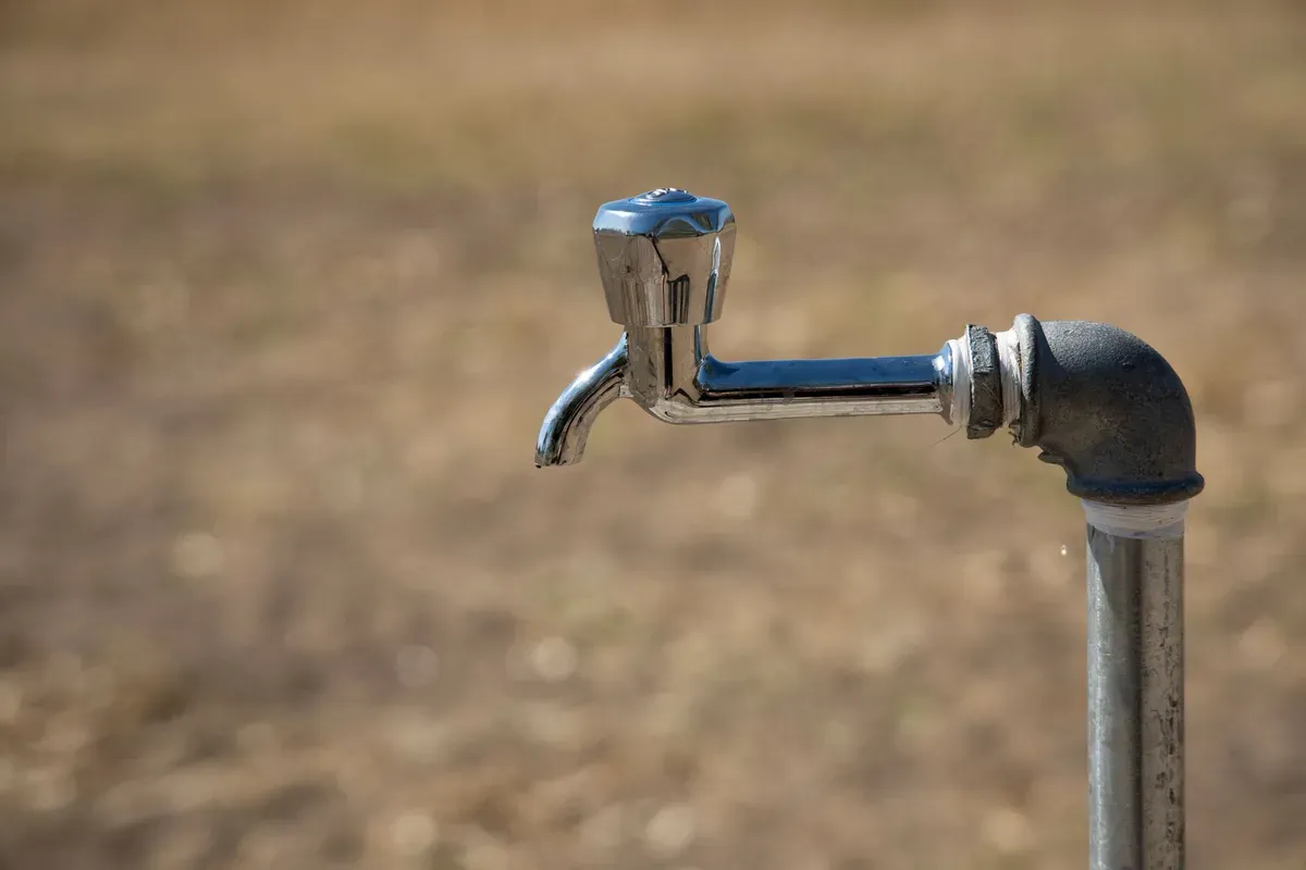 Dry water tap mounted on metal pipe against dusty ground, symbolizing water scarcity