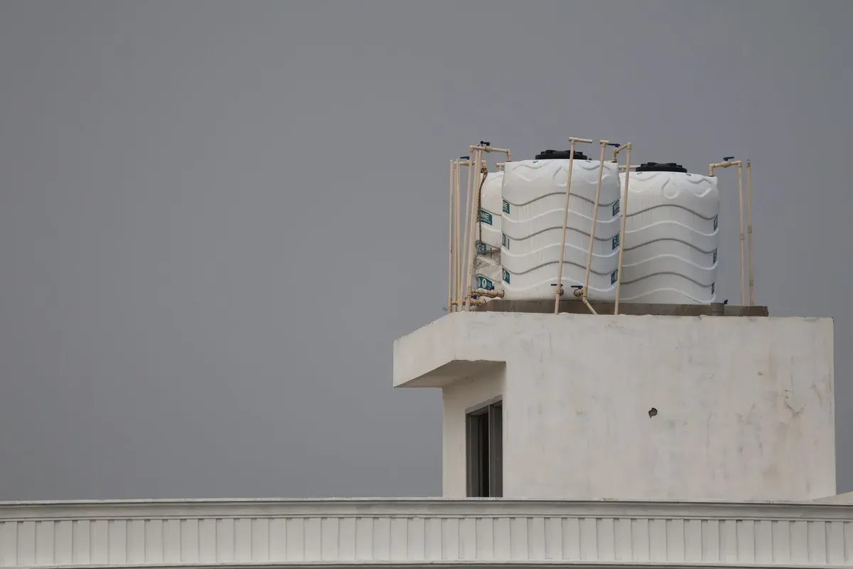 Two white plastic water storage tanks installed on roof platform of residential property with metal support frame