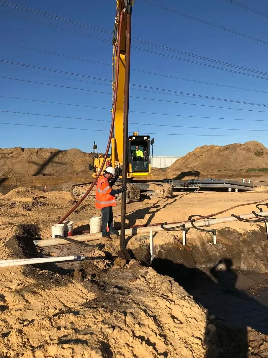 Wellpoint drilling rig with operator in safety vest performing installation on construction site with excavated ground