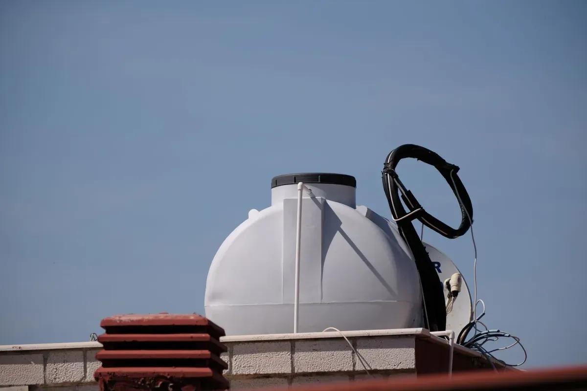 White spherical water storage tank mounted on residential rooftop platform with black valve and pipe connections