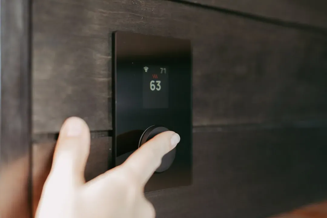 Hand touching a smart home monitoring device with digital display showing temperature reading and Wi-Fi icon