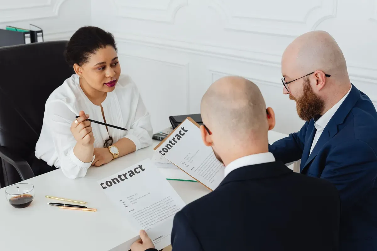 Three business professionals reviewing contract documents at a desk in an office