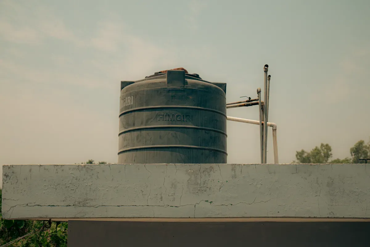 Cylindrical water storage tank with visible inlet and outlet pipes mounted on concrete platform