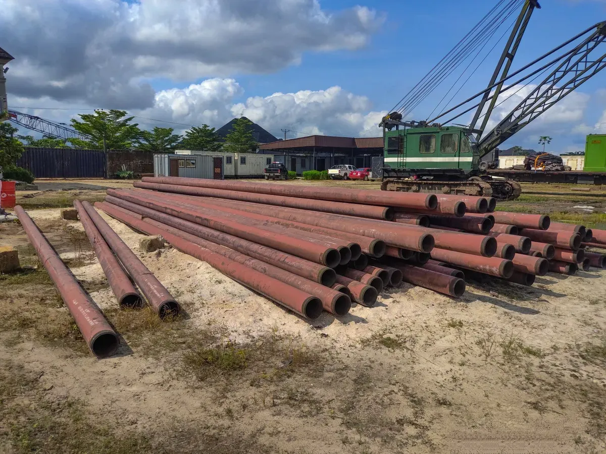 Industrial steel bore casing pipes stacked at a South African water infrastructure jobsite with crane and work vehicles visible