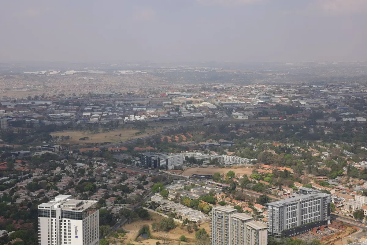 Aerial view of upmarket Johannesburg northern suburbs with modern residential tower blocks, green spaces, and sprawling suburban development under hazy sky