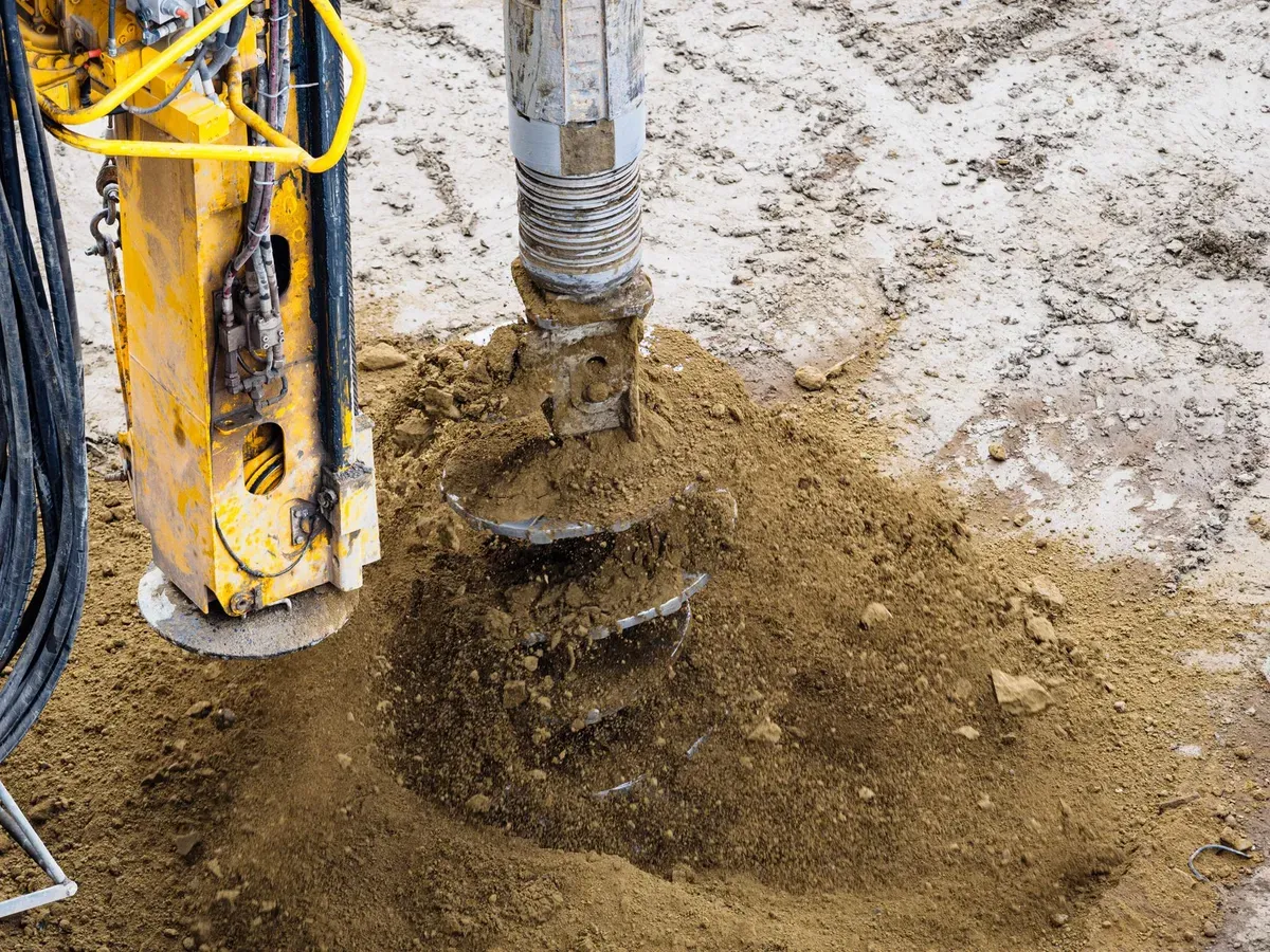 Yellow drilling rig bore-drilling into ground with pipe and hydraulic systems visible at suburban jobsite