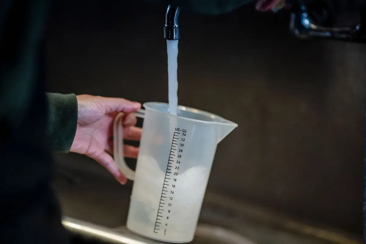 Person holding measuring jug with graduation scale while water flows into it from a tap