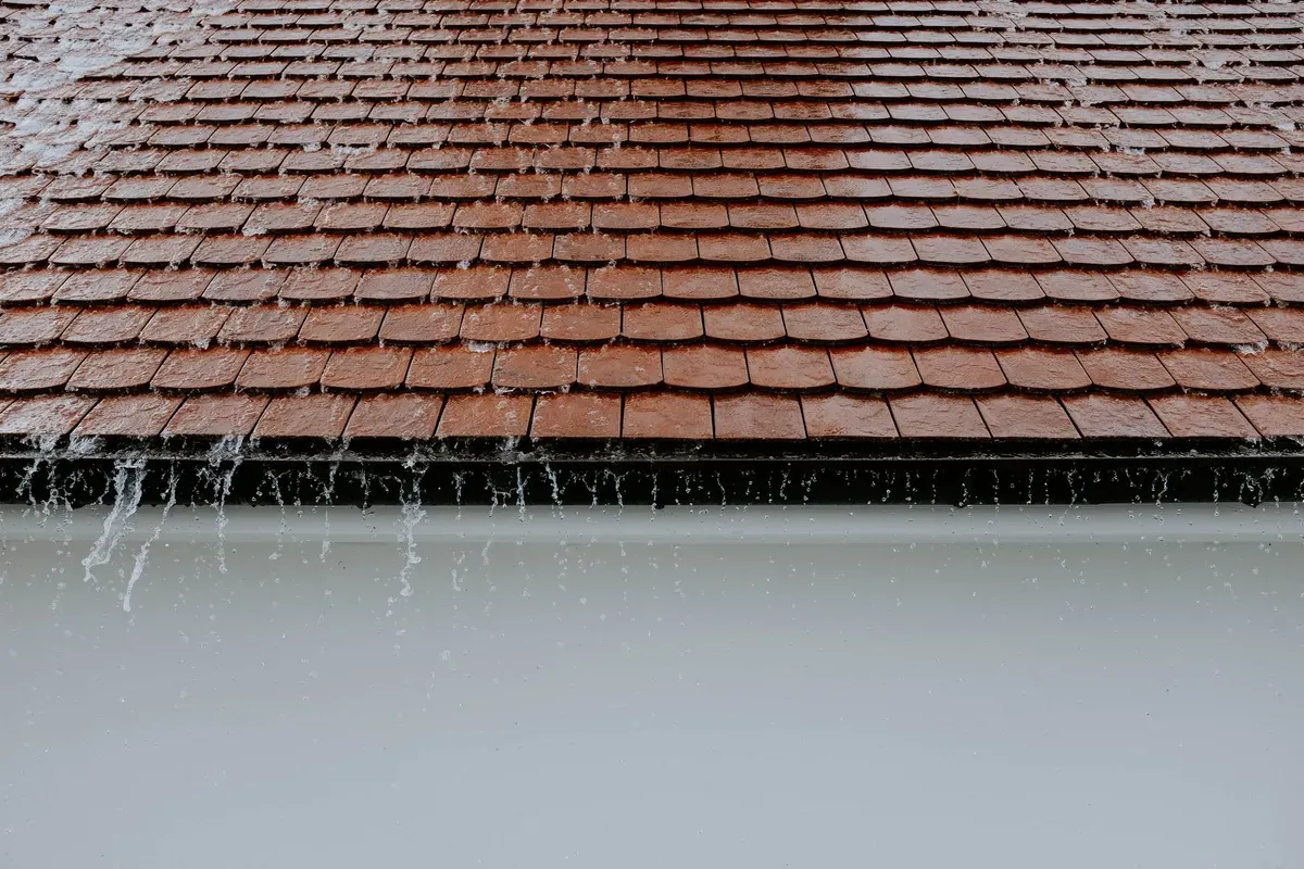 Clay tile roof with metal gutters and downpipe showing water flowing during rainfall