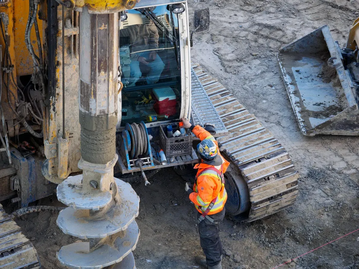 Borehole drilling rig with operators in safety gear managing drill pipes and equipment on active construction site